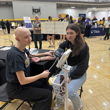 A student administering a blood pressure screening to a fair attendee. 